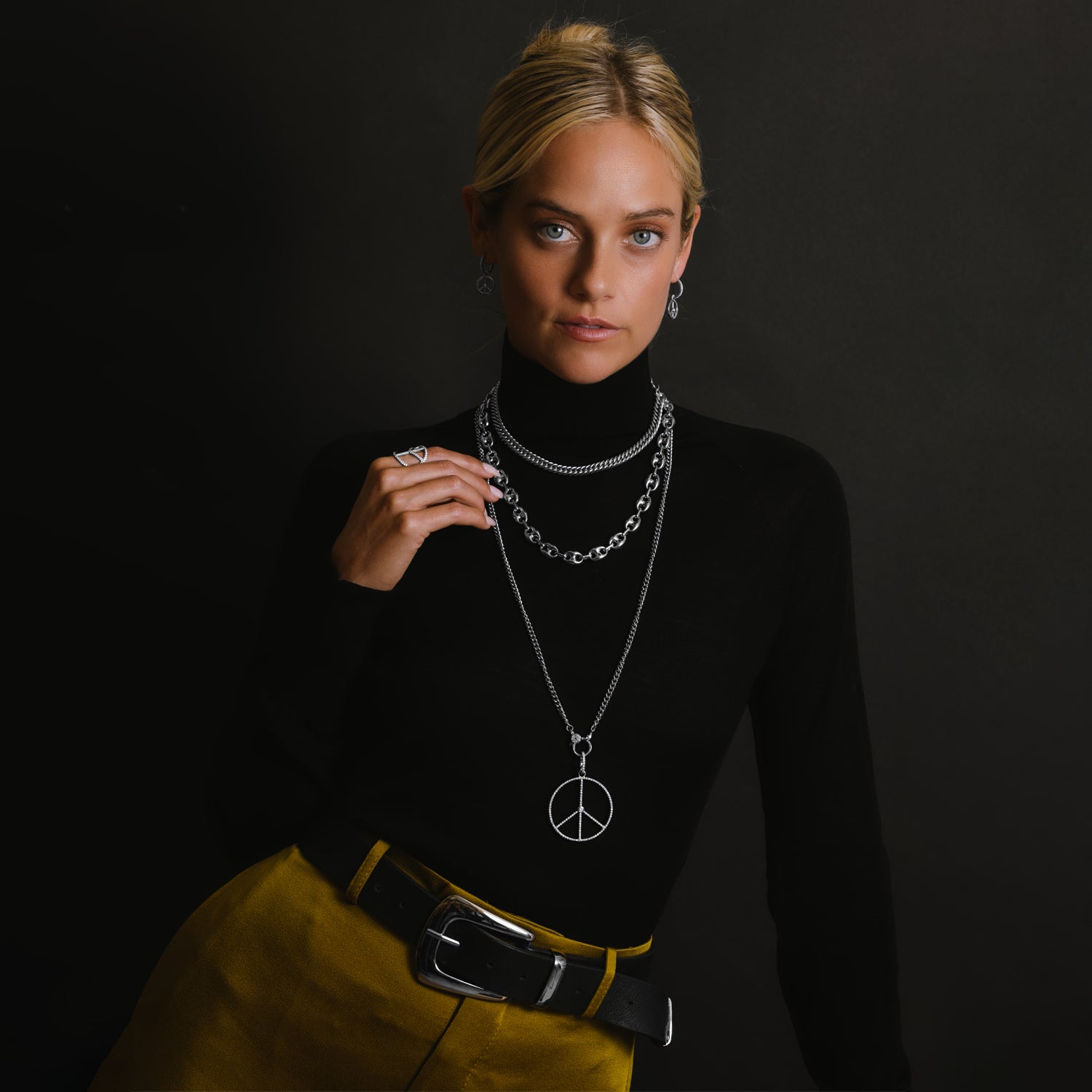 Sheryl Lowe sterling silver signature jewelry pictured on a model in a black top. Jewelry includes curb chain, mariner chain, peace sign necklace, peace sign ring and peace sign earrings.