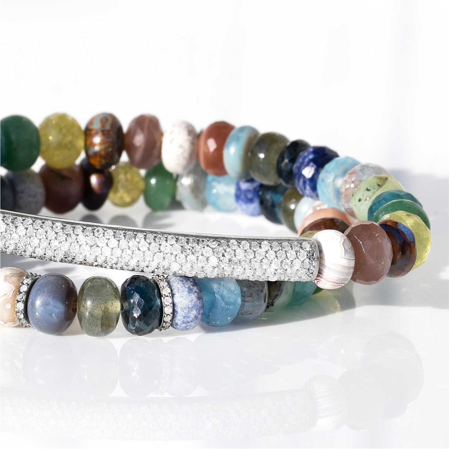 Two stacked multi colored gemstone bead bracelets. The top bracelet features a diamond bar and the bottom bead bracelet features diamond rondelles.