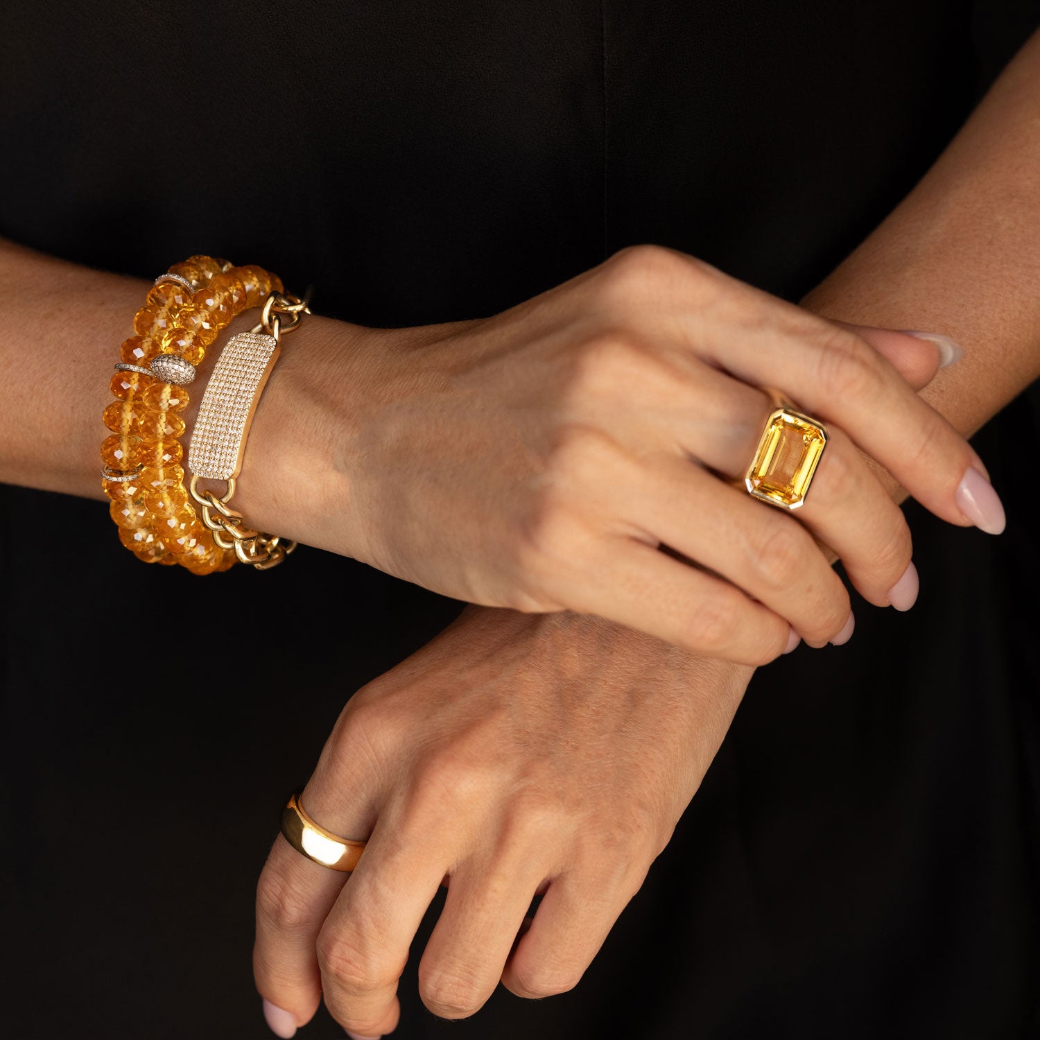 Three Sheryl Lowe bracelets (2 citrine bead bracelets and a 14k gold and diamond ID bracelet) stacked on a woman's wrist and a citrine and 14K gold cocktail ring on her middle finger.